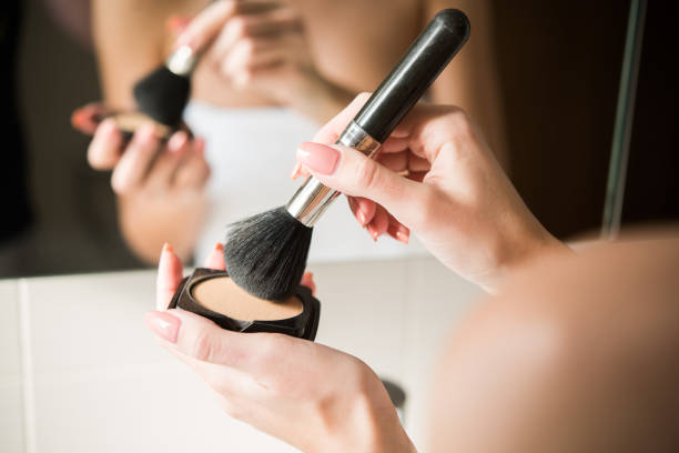 A close up shot of a woman in a bathroom putting powder on a make up brush.